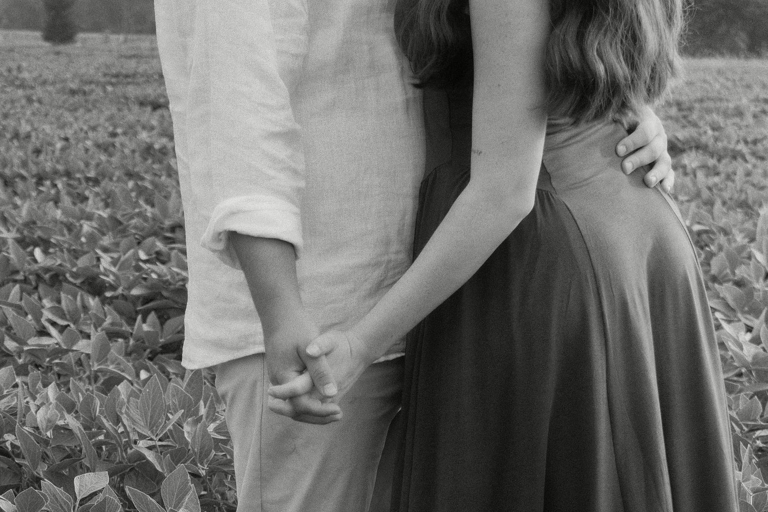 Black and white photo of a couple holding hands in a field, woman in flowing dress, man in white linen shirt.