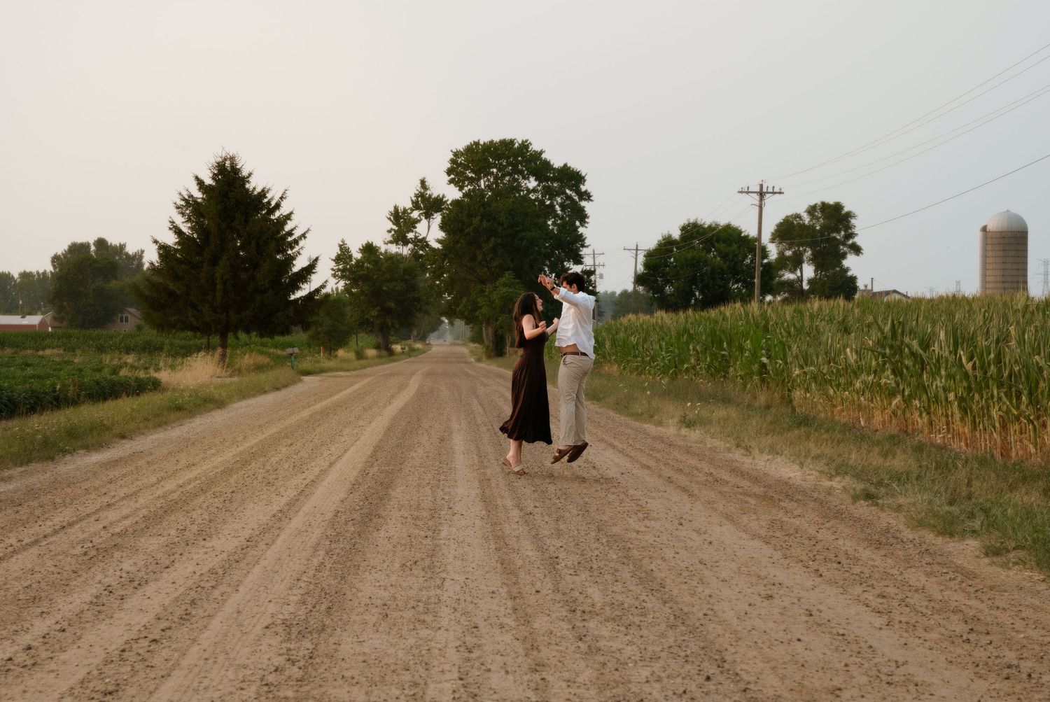 Couple dancing together on rural dirt road surrounded by cornfields and farm scenery.