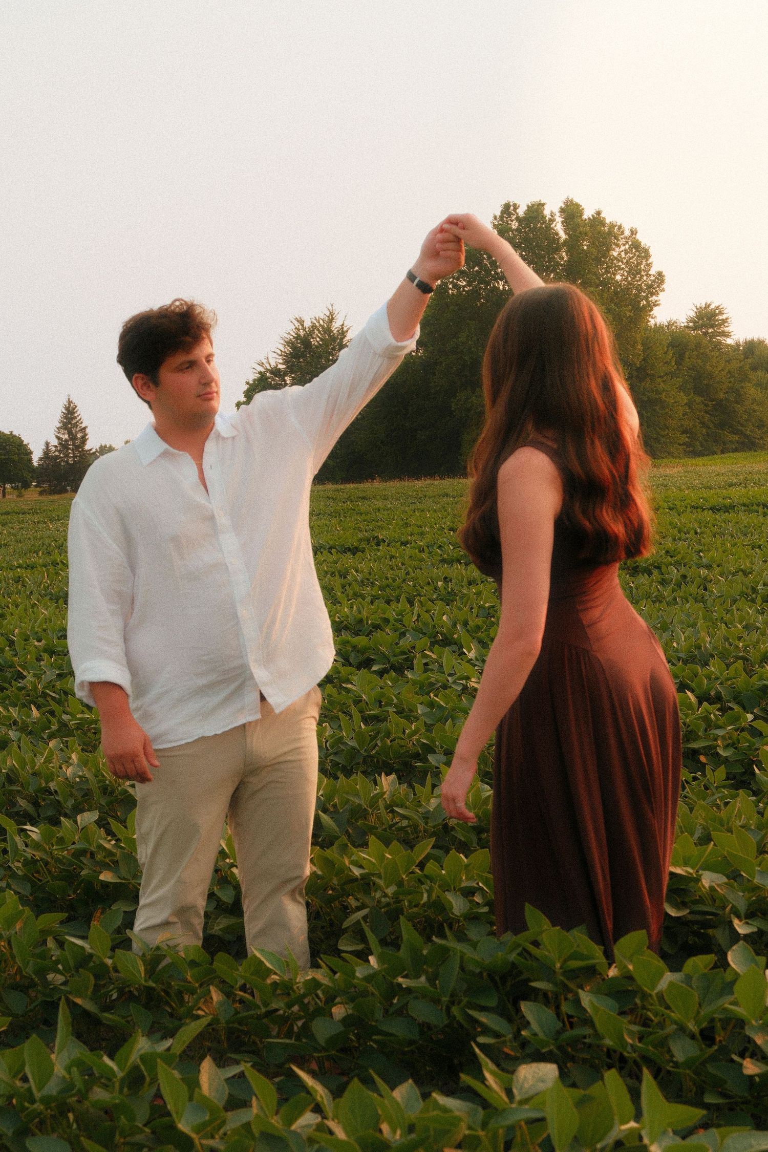 A couple dances together in a lush green field, man in white shirt raising woman's hand in a twirl at sunset.