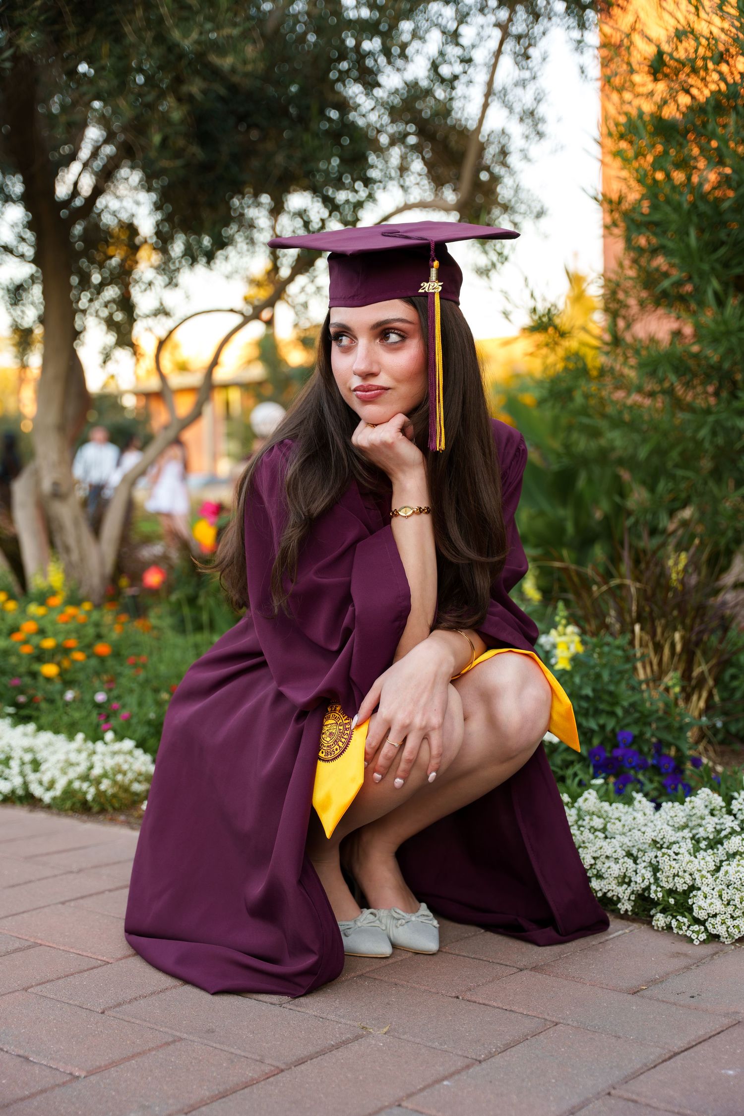 girl posing by some flowers in her graduation regalia