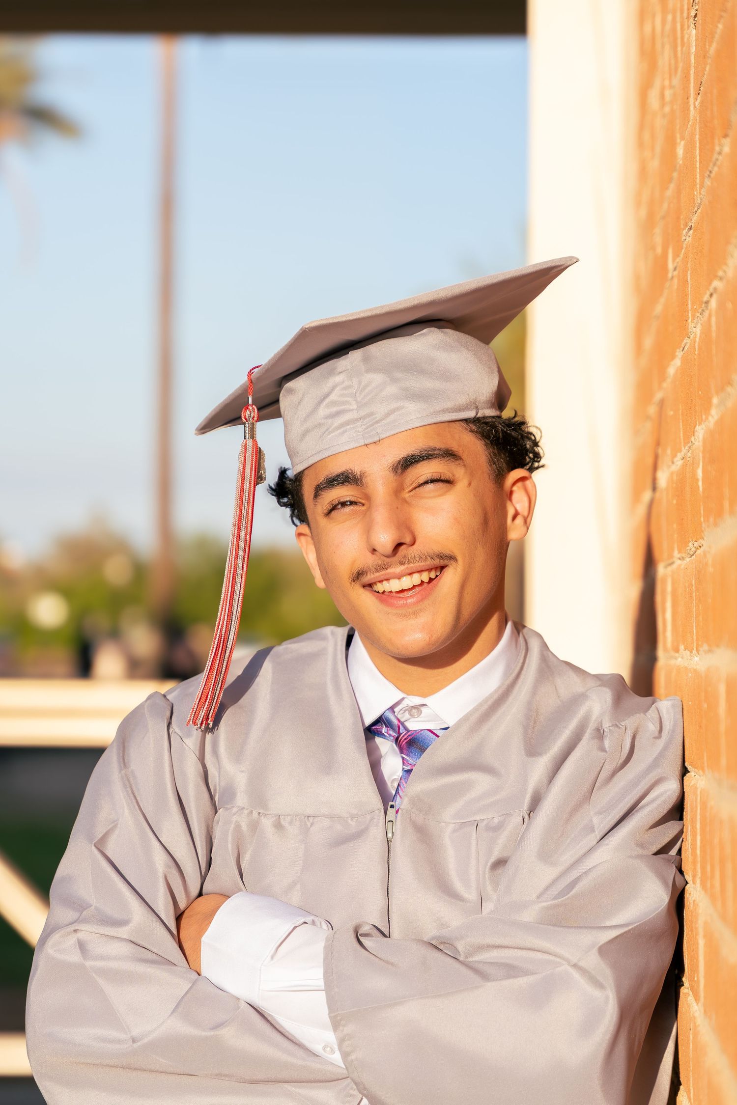 boy poses in his regalia leaning on a brick wall