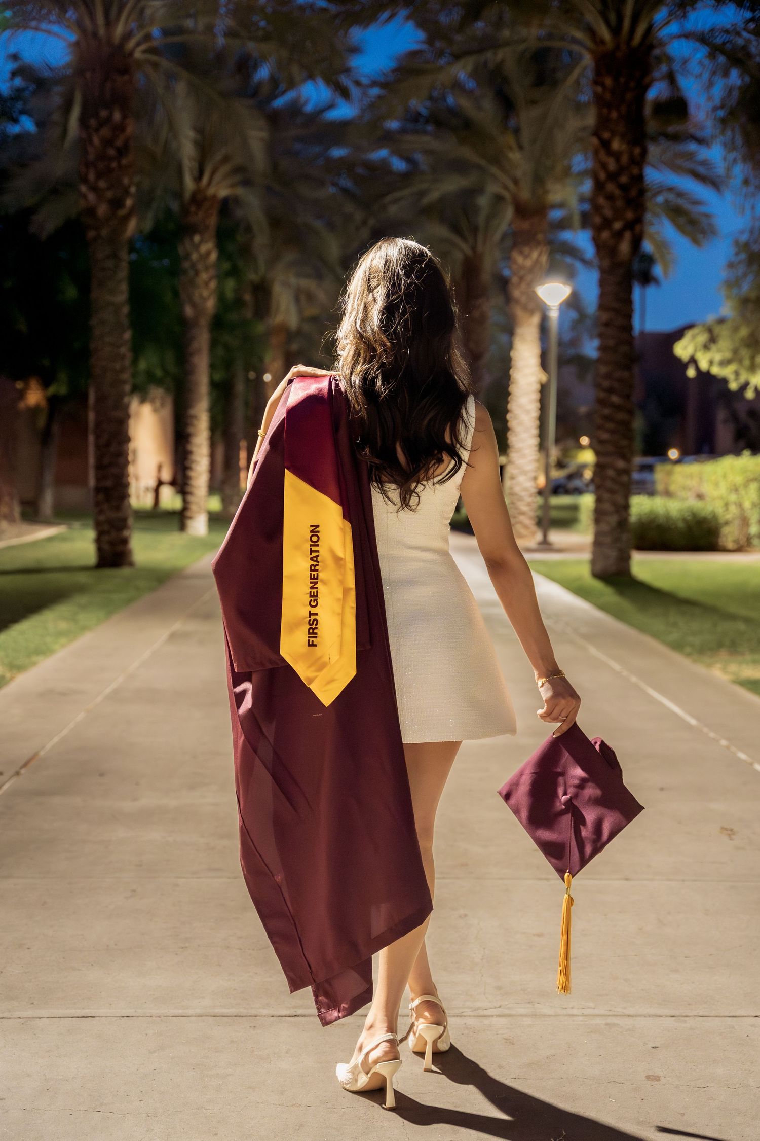 woman walking away with her regalia on her back and cap in her hand