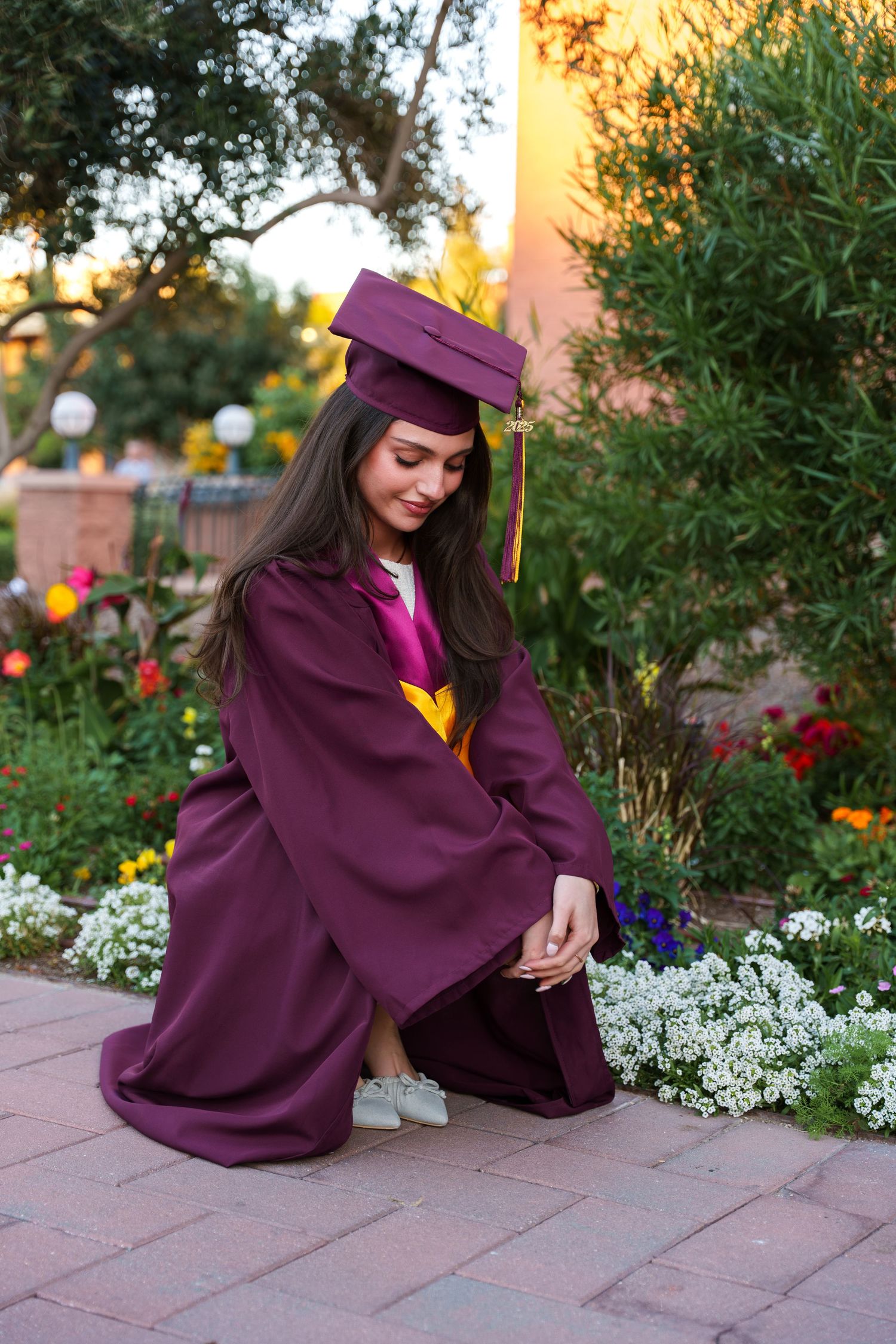 girl posing by some flowers in her graduation regalia