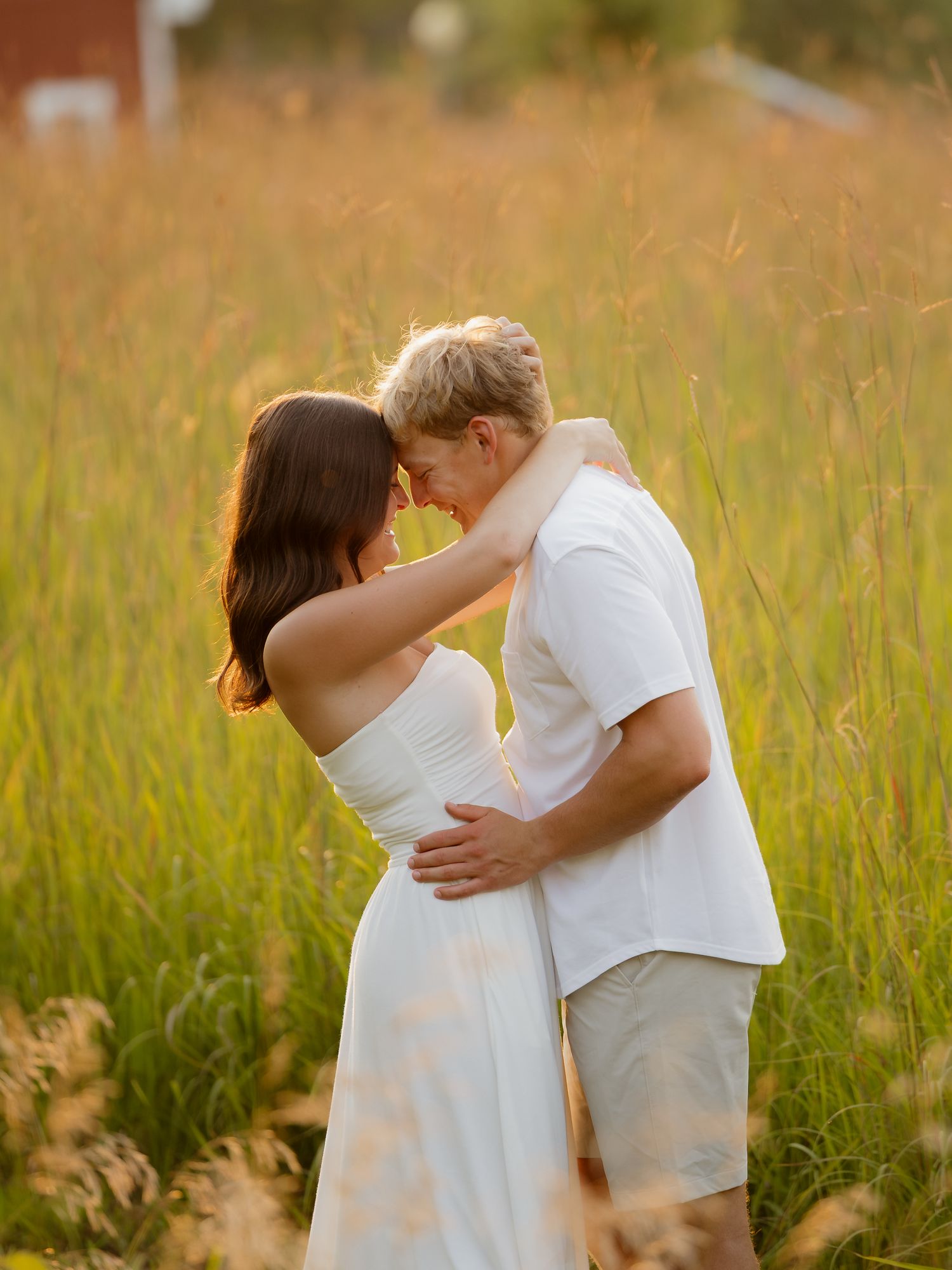 Couple in white embracing in golden field at sunset, romantic outdoor engagement photo.