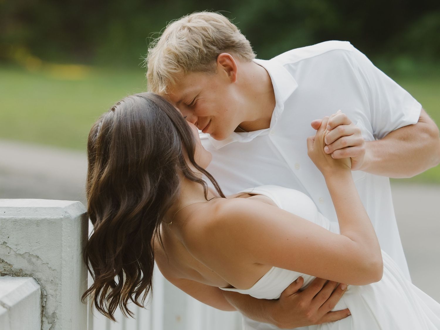 Couple sharing a romantic dip kiss near a white fence during an outdoor engagement photoshoot in Minnesota.