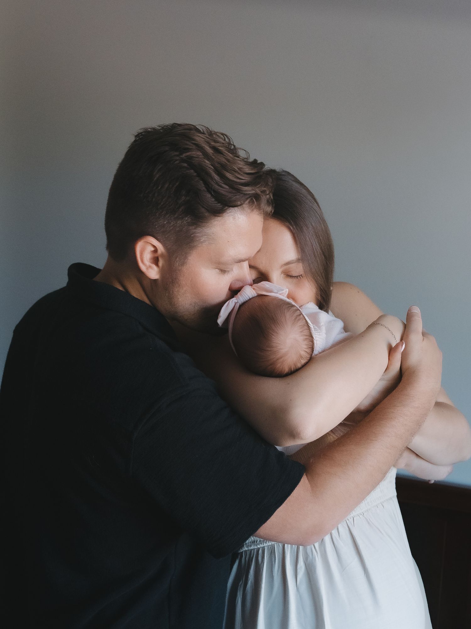 Parents tenderly embracing newborn baby together in soft indoor portrait.