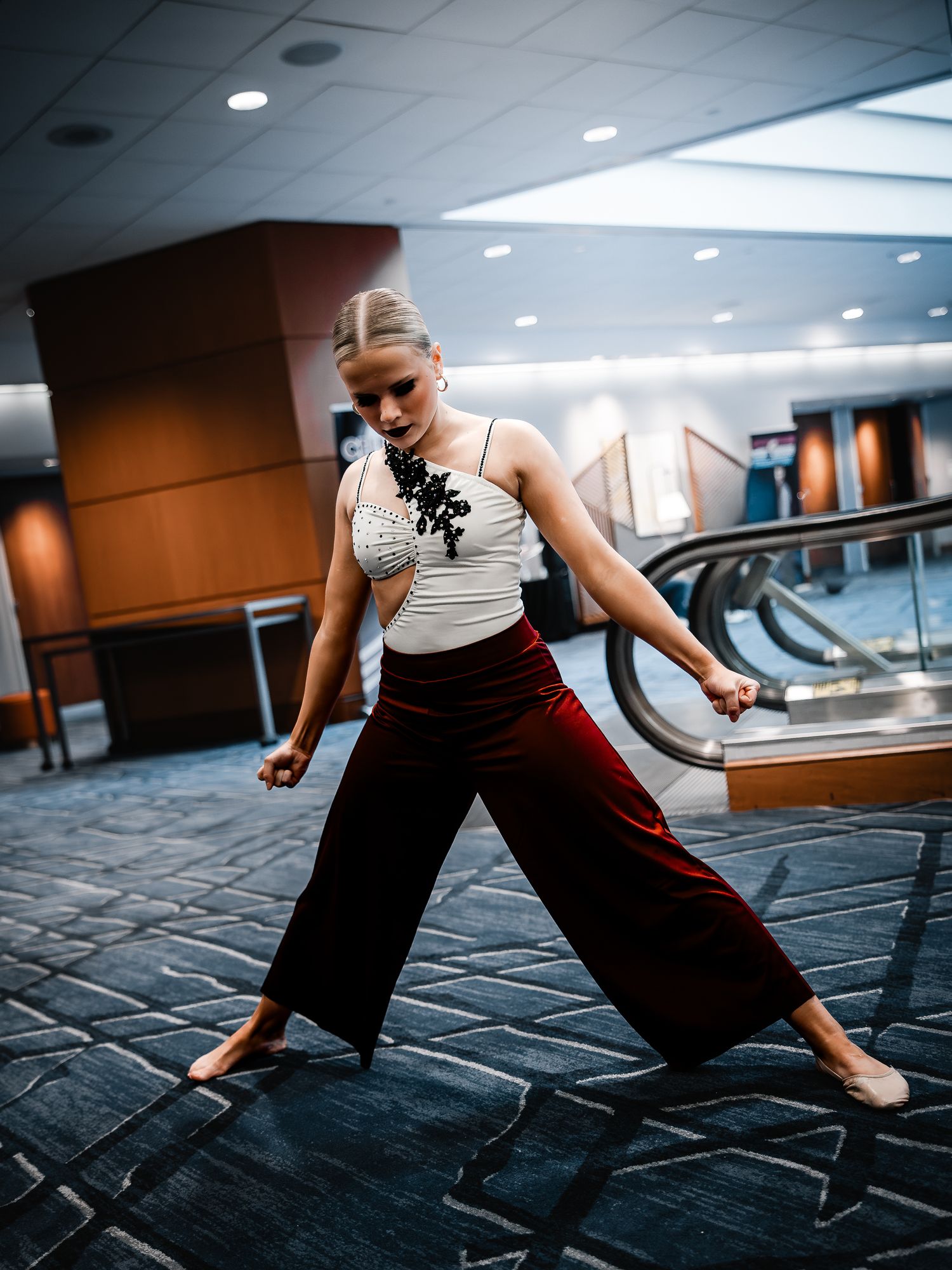 Dancer performing contemporary dance moves in wide-leg burgundy pants and white top indoors.
