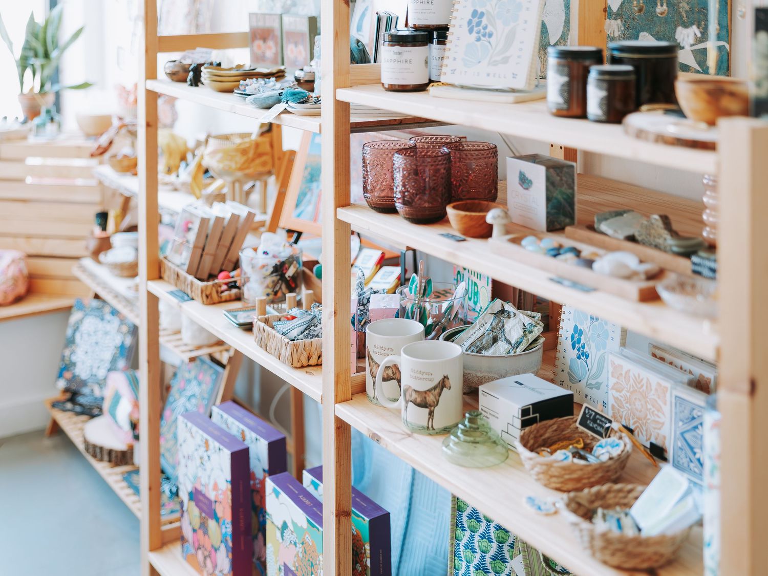 Wooden shelving unit with artisan goods, candles, stationery, and handmade crafts in shop.