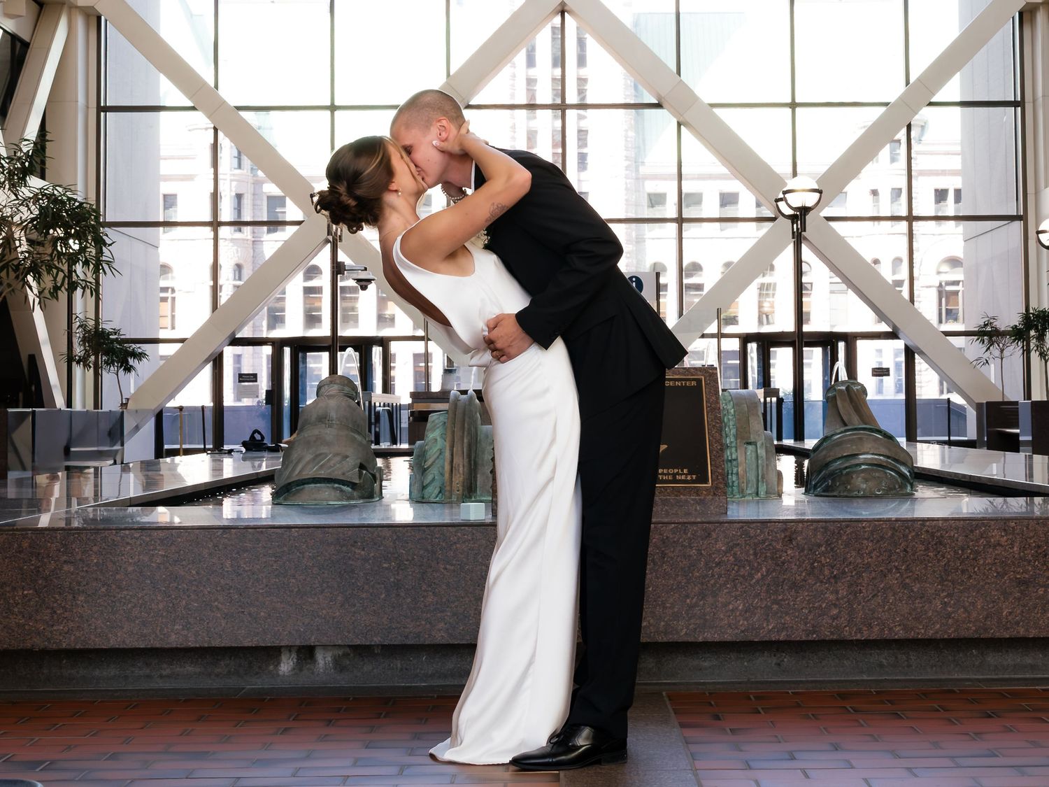 Bride and groom share a romantic kiss in an elegant indoor venue, bride wearing a white gown and groom in a black tuxedo.