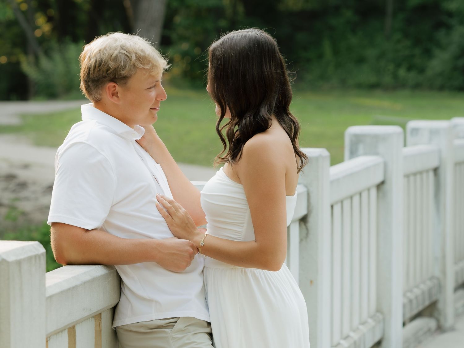 Couple in white outfits sharing a romantic moment on a wooden bridge surrounded by lush greenery.