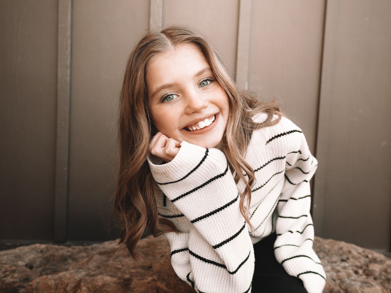 Cheerful young girl in striped sweater smiling brightly while posing casually indoors.