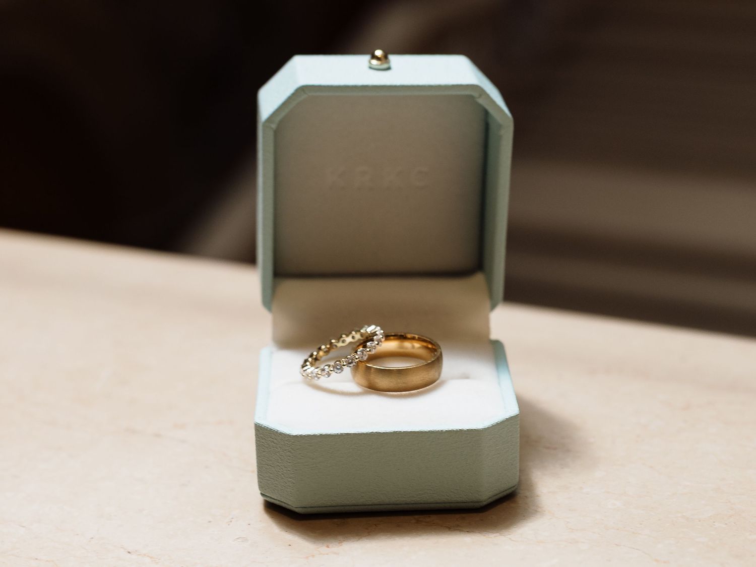 Two wedding rings displayed in an elegant mint green ring box, one gold band and one diamond.