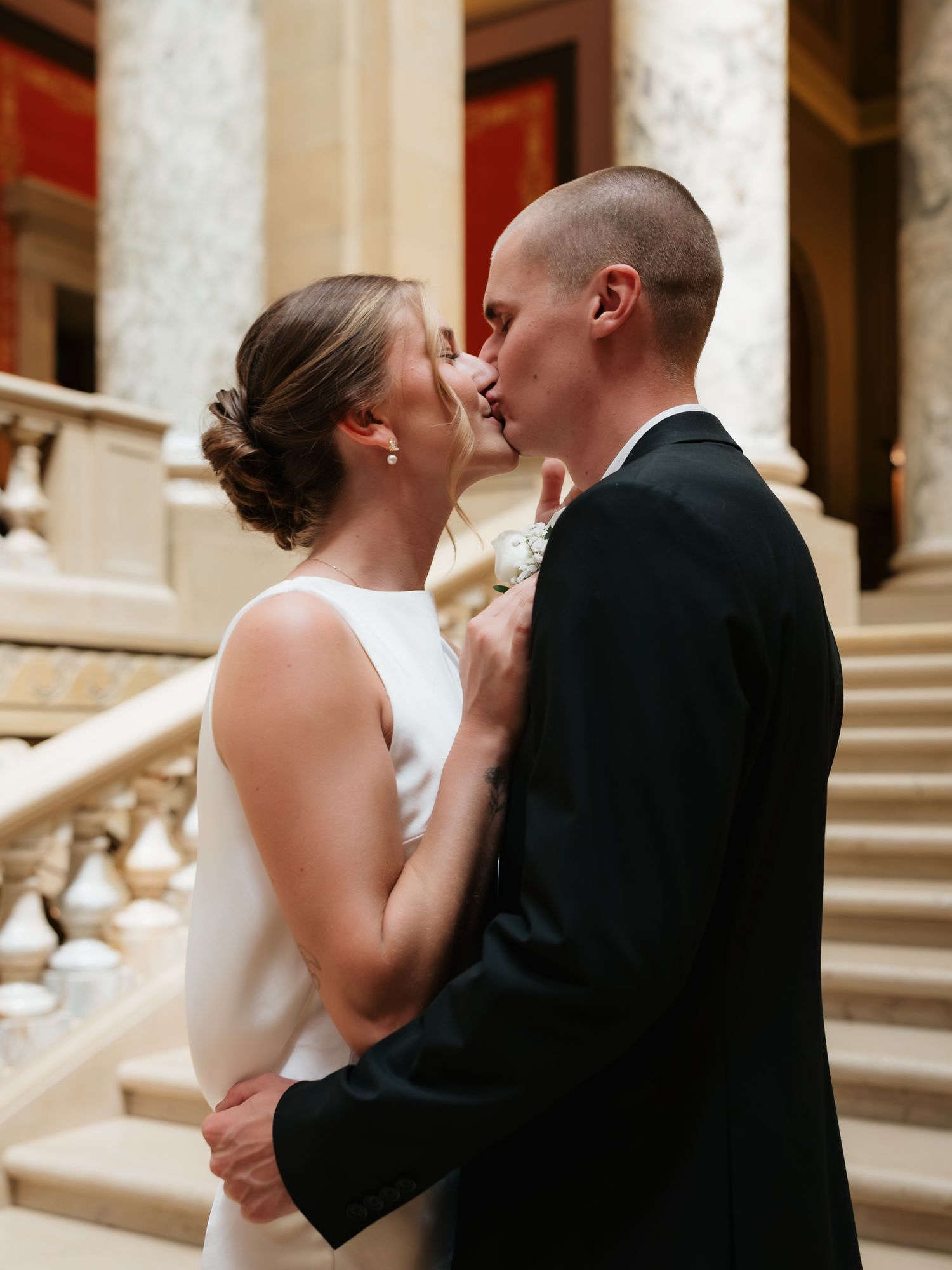 A bride and groom share a romantic kiss on an elegant staircase in a grand venue on their wedding day.