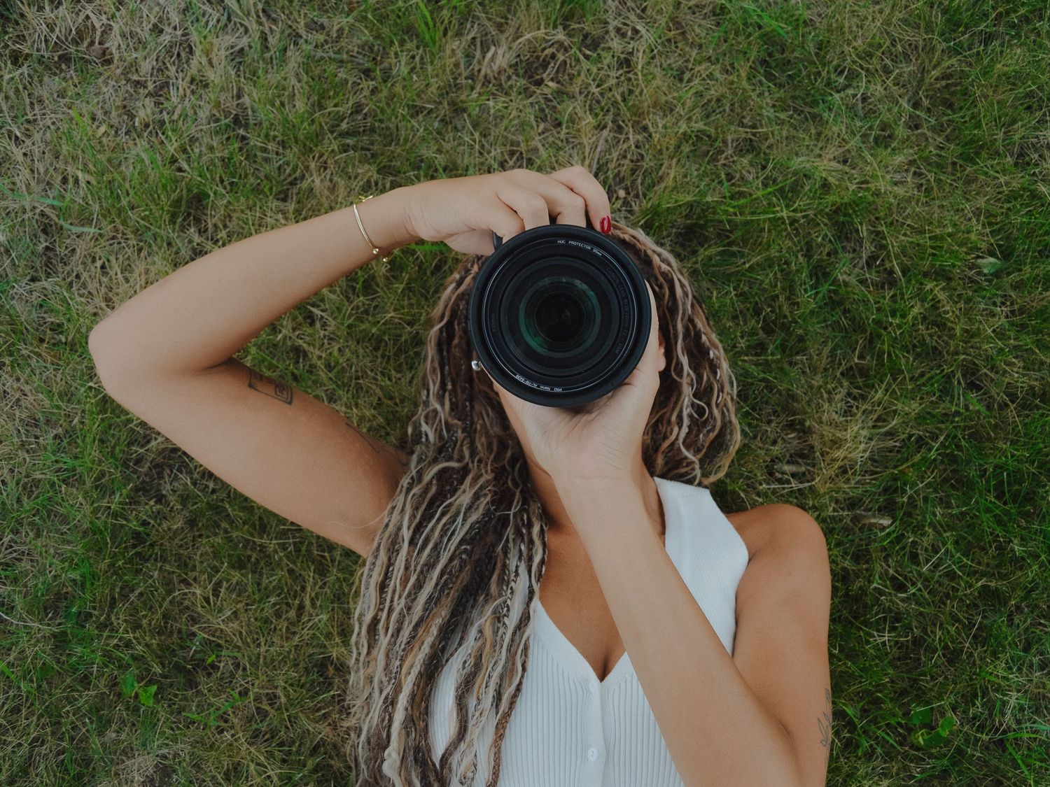 Overhead view of woman lying on grass holding camera up to face with braided hair spread out.