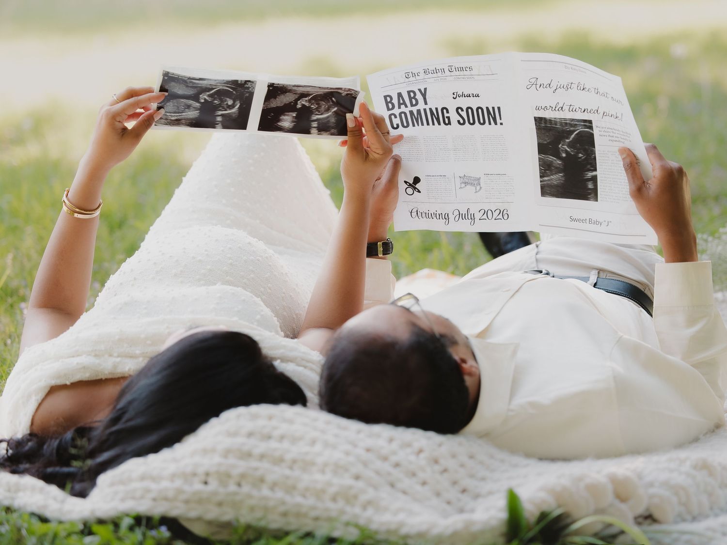 Expecting couple lying on blanket reading baby coming soon newspaper announcement outdoors.