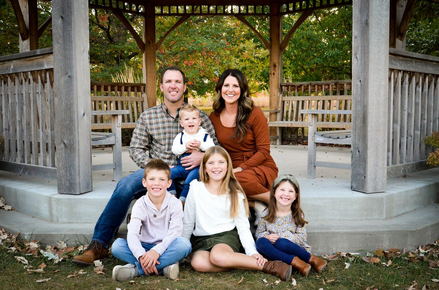 Happy family of six posing under a gazebo in autumn park with four children and two parents.