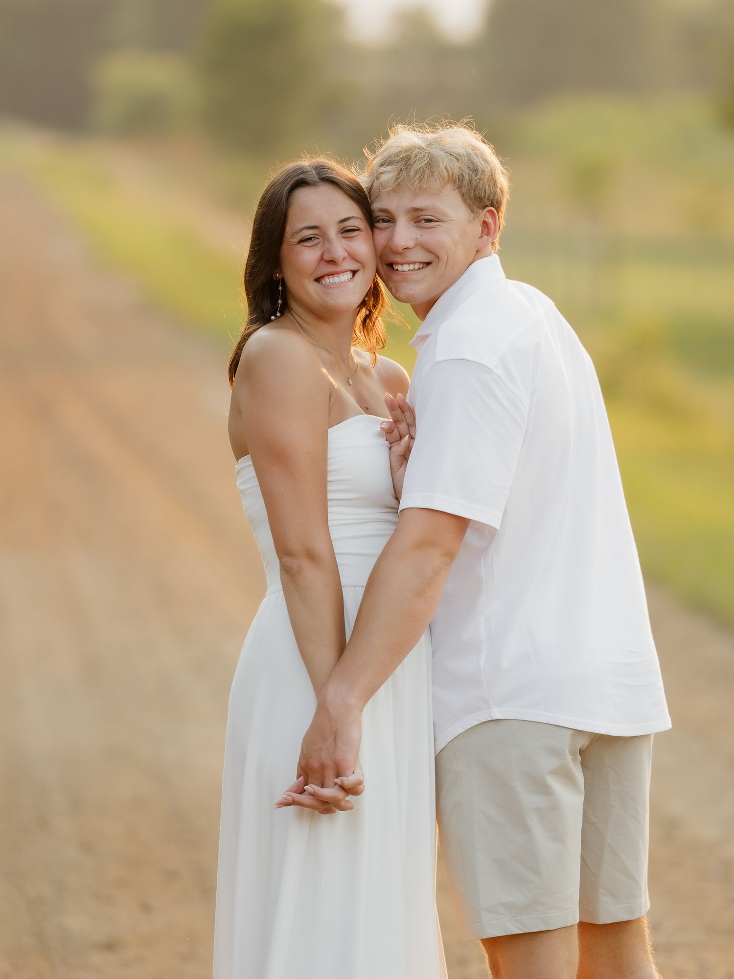 Smiling couple holding hands on a dirt road at sunset during golden hour engagement photo session.