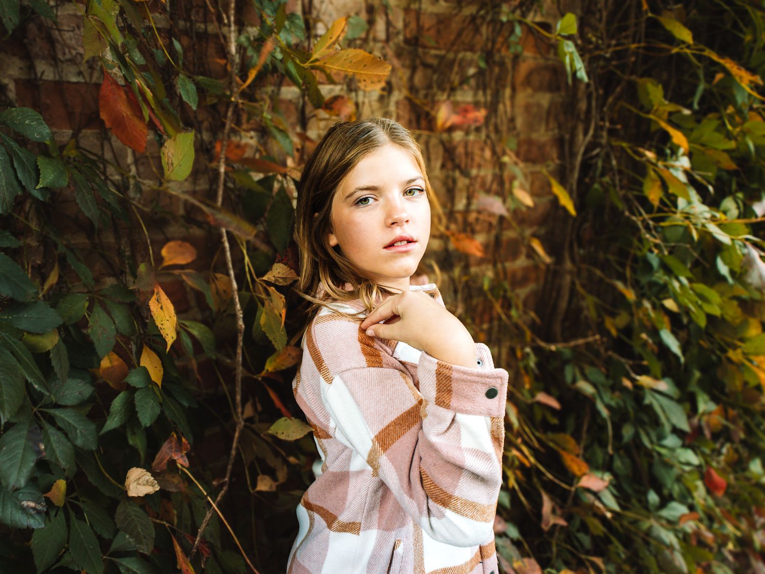 Young woman in plaid shirt posing thoughtfully in front of colorful autumn foliage.
