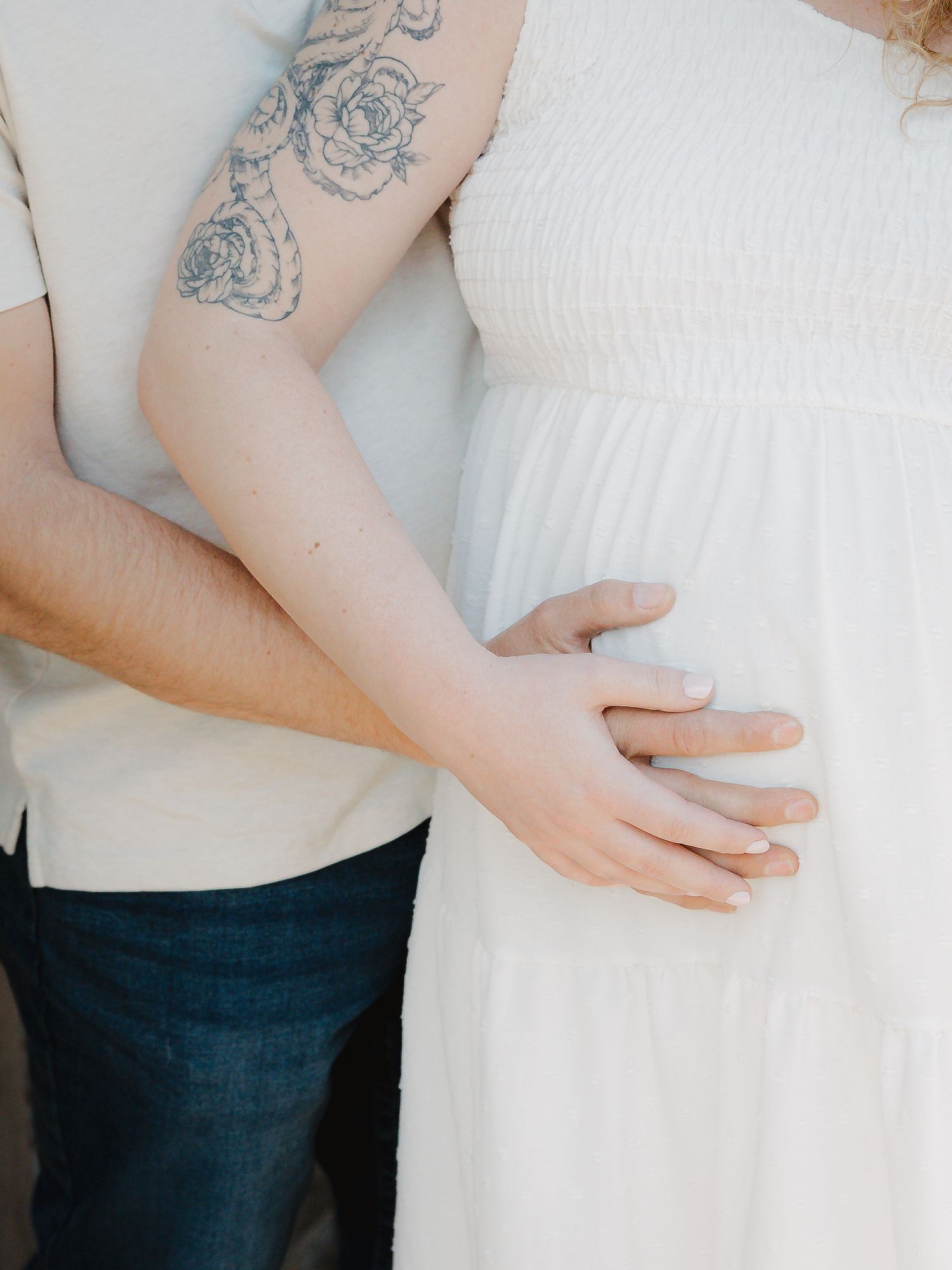 A couple shares a tender moment as a tattooed man rests his hand on a pregnant womans belly.