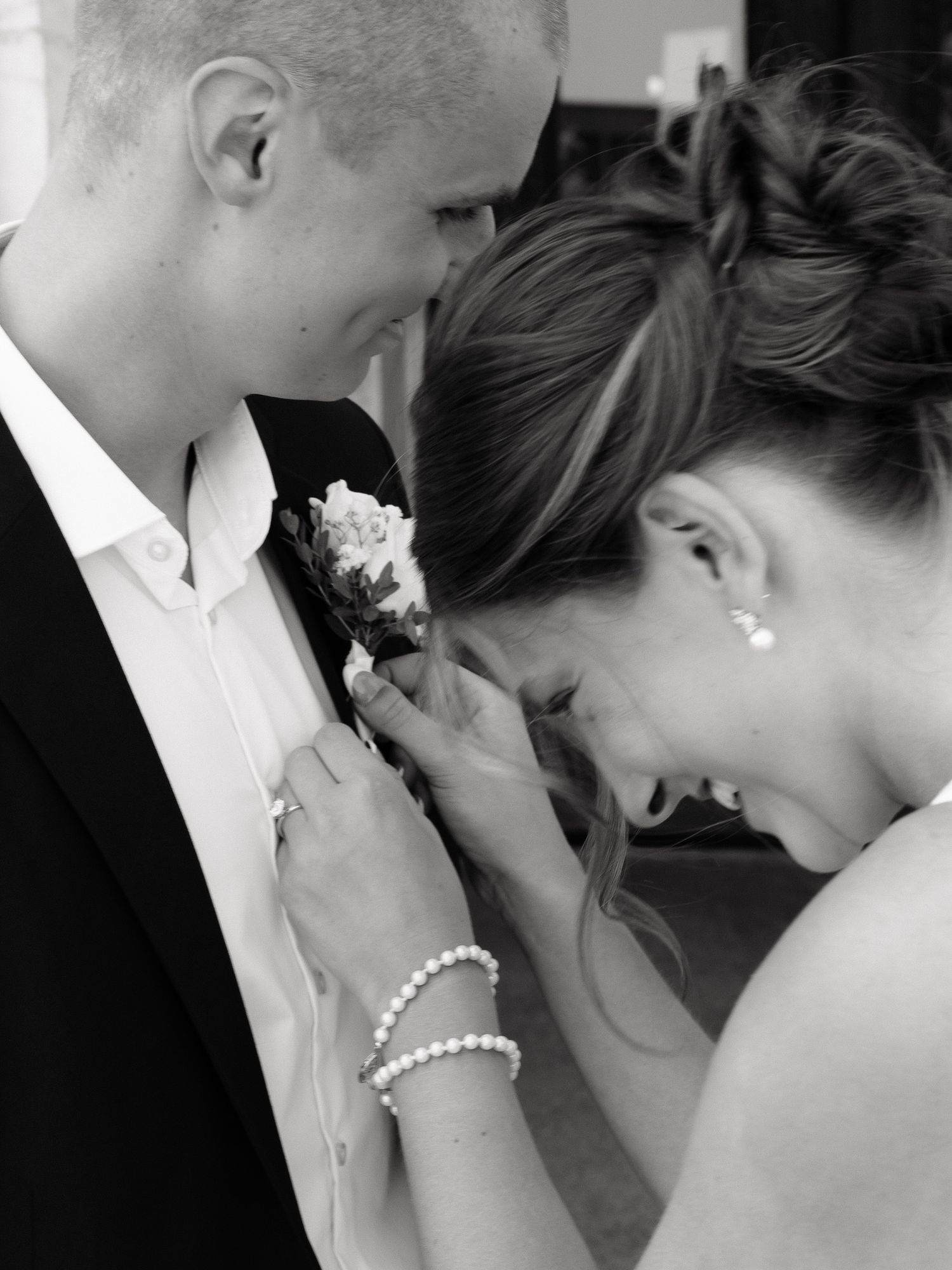 Bride pinning boutonniere on groom's lapel in black and white wedding photo.
