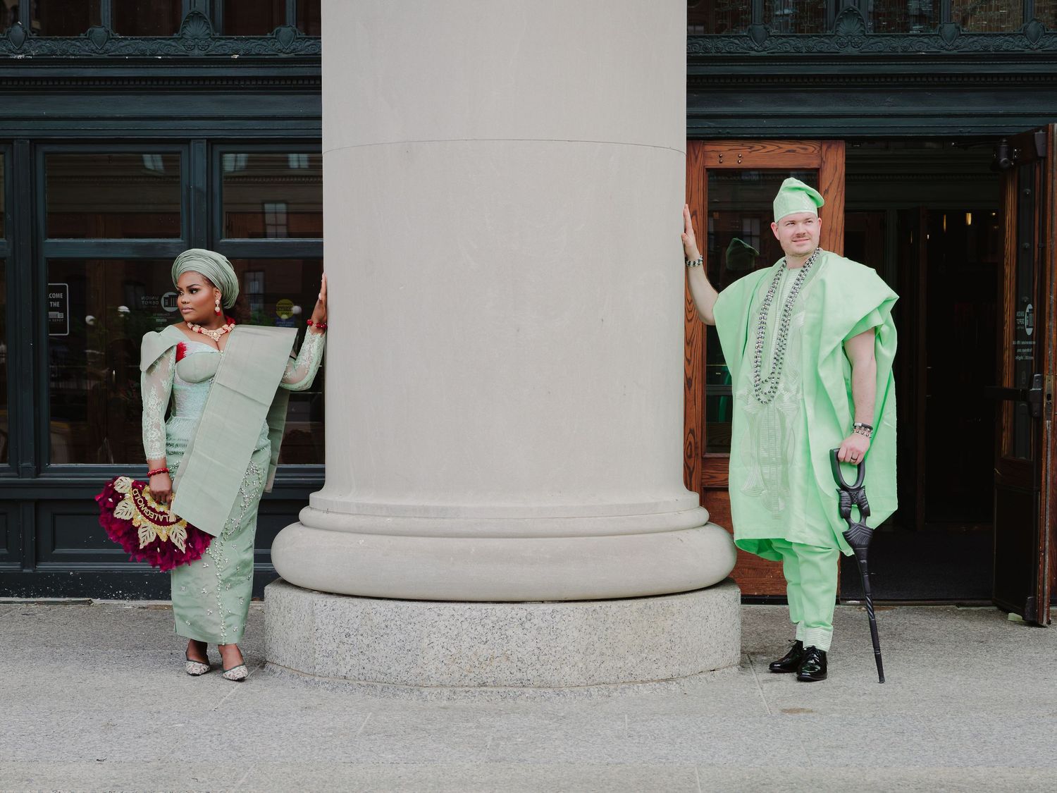 Man and woman in elegant mint green traditional garments posing near architectural column.