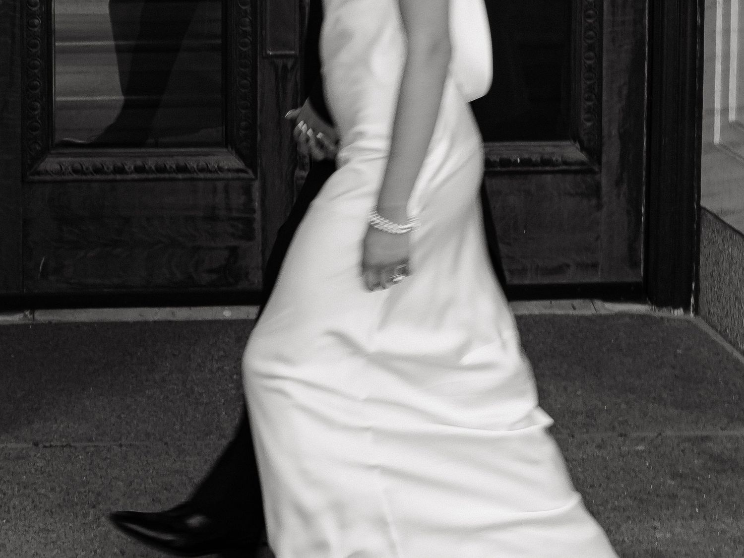 Bride in elegant white gown walking outside building in black and white photo.