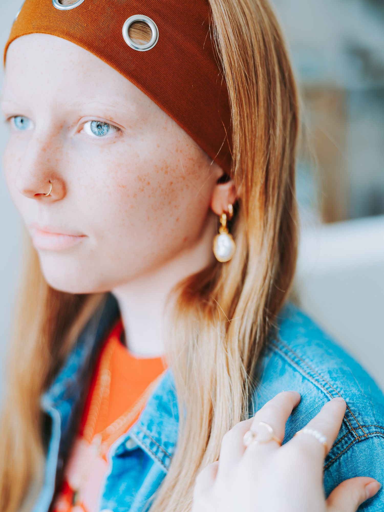 Close-up of redhead woman with freckles wearing pearl earring, nose ring, and headband.