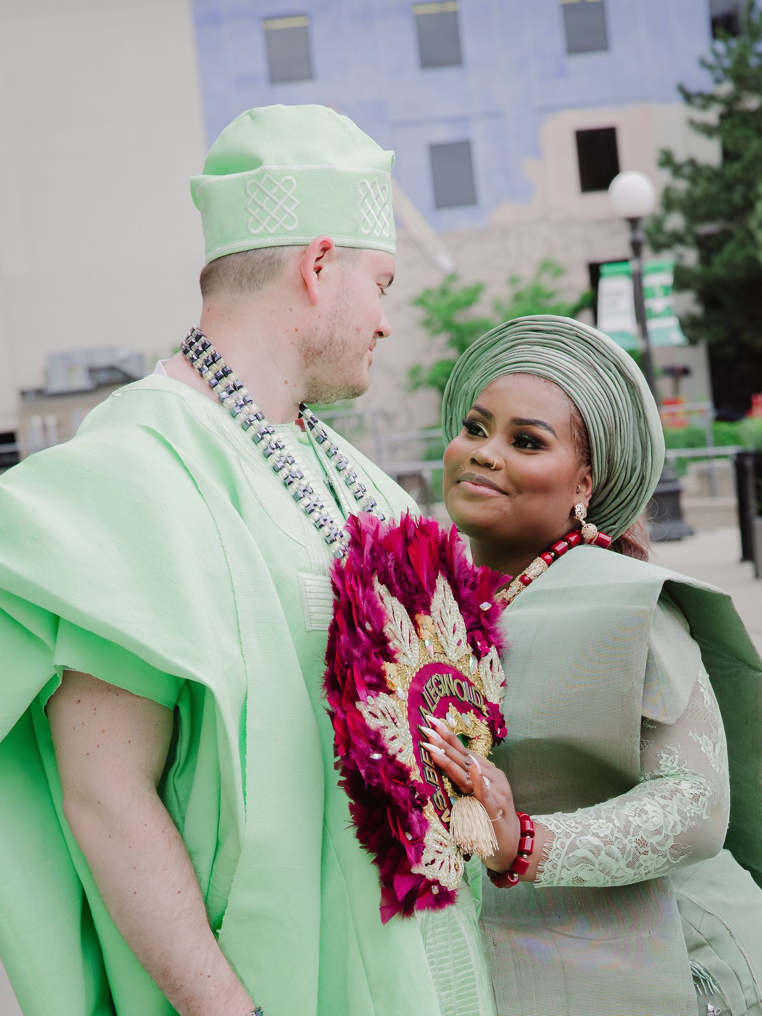 Couple in matching mint green traditional Nigerian wedding attire smiling at each other outdoors.