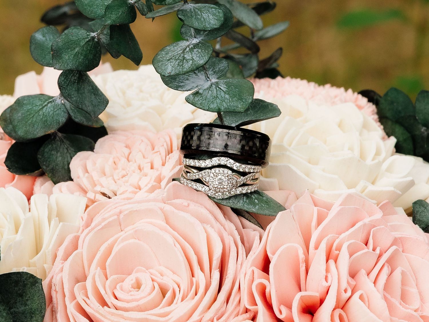 Wedding rings displayed on pink and white rose bouquet with eucalyptus greenery.