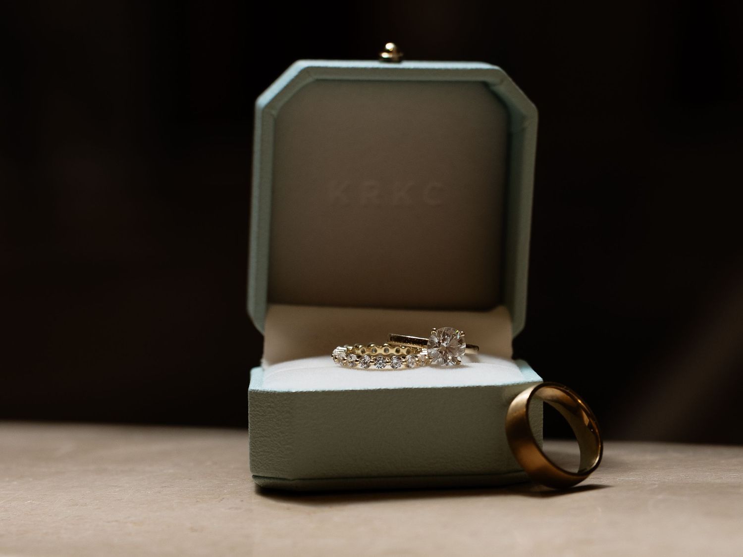 Diamond engagement ring and gold wedding band displayed in a teal VRAI jewelry box.