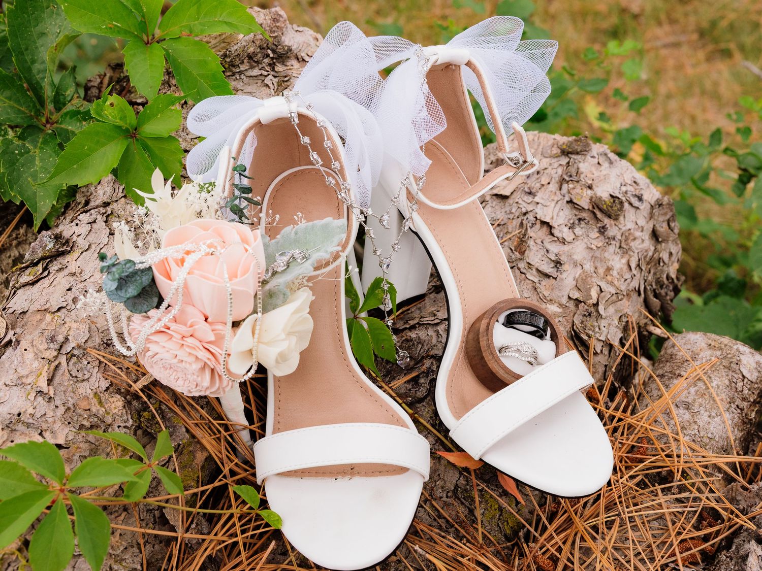 White bridal heels with floral accents displayed on rustic wood outdoors.