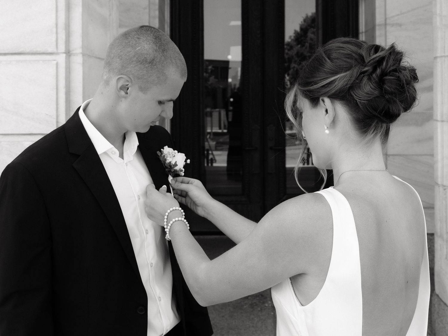 Black and white photo of bride pinning boutonniere on groom's lapel before wedding ceremony.