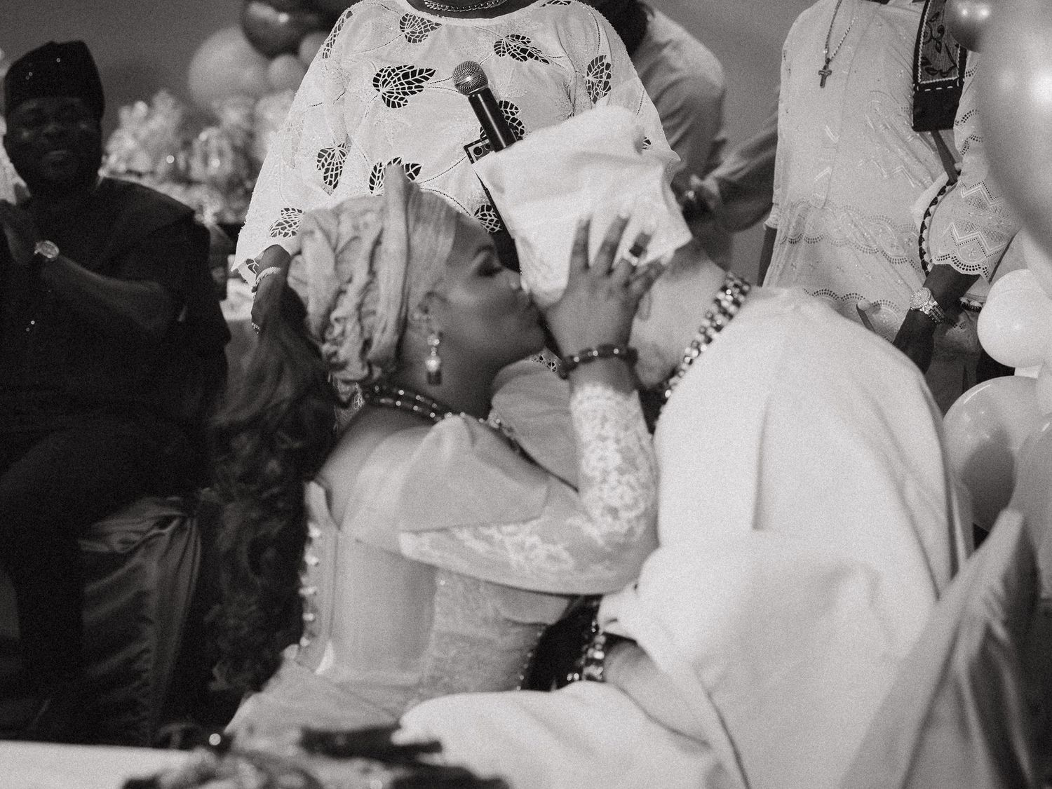 Black and white photo of couple sharing a kiss at a traditional African wedding celebration.