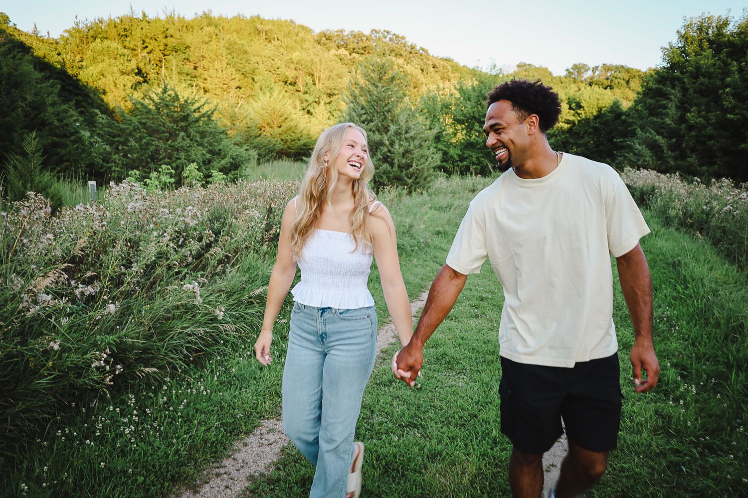 Happy interracial couple laughing and holding hands while walking on a scenic green nature path.