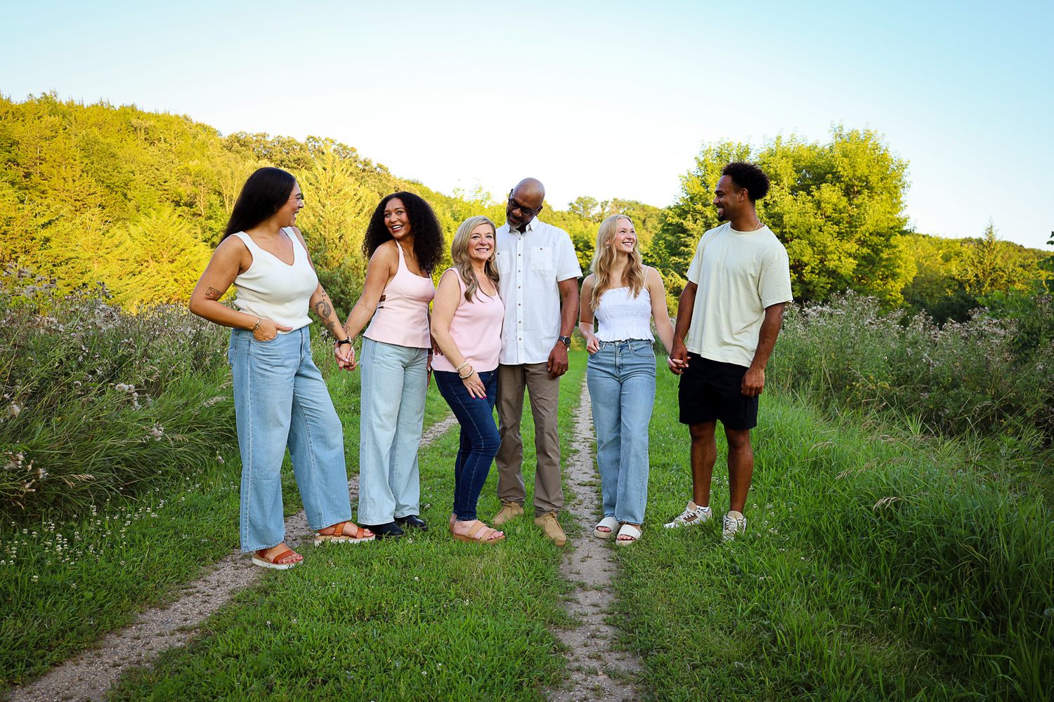 Group of six friends walking together on a nature trail surrounded by lush green summer foliage.