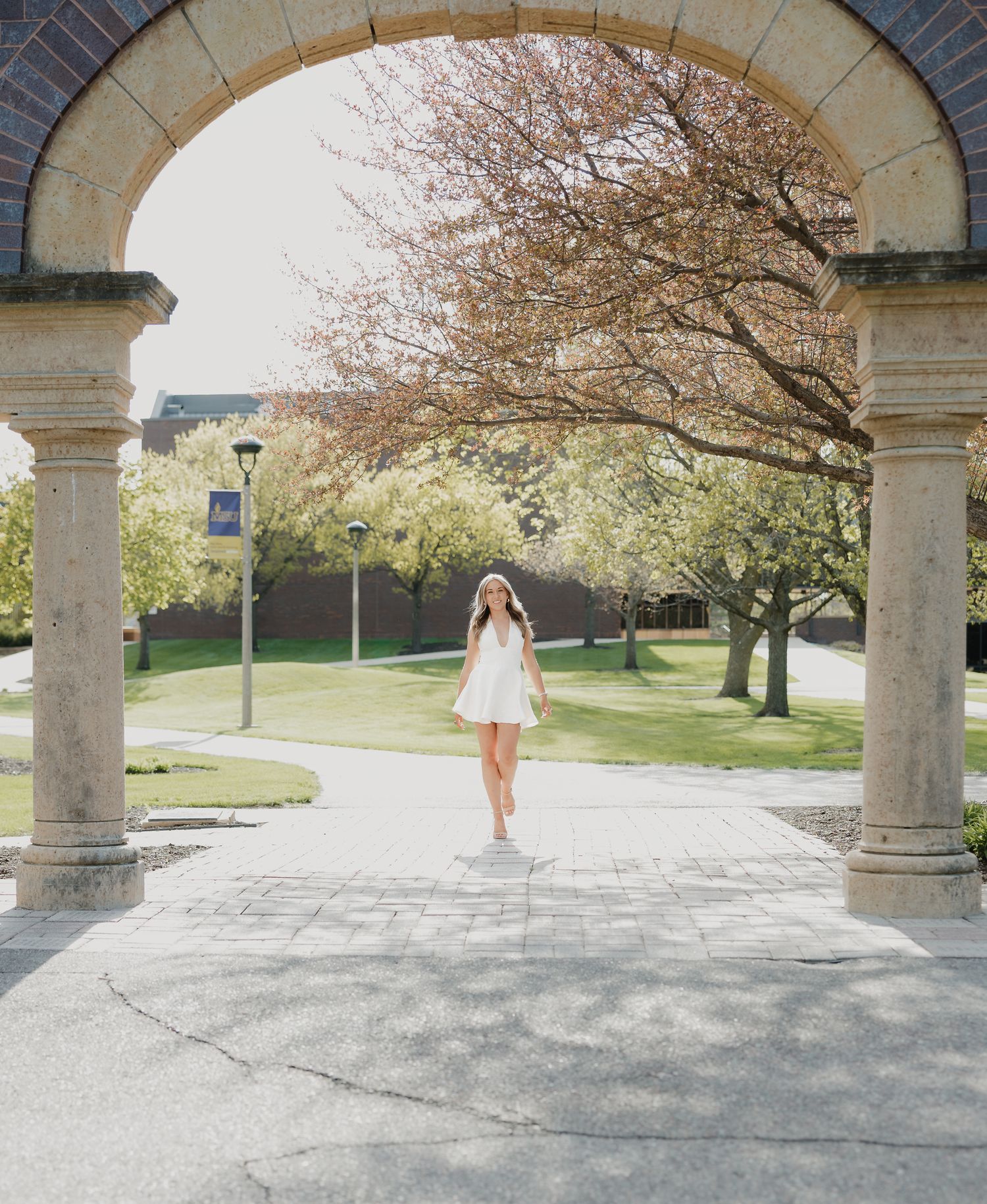 Woman in white dress framed by stone arch on a bright sunny campus walkway.