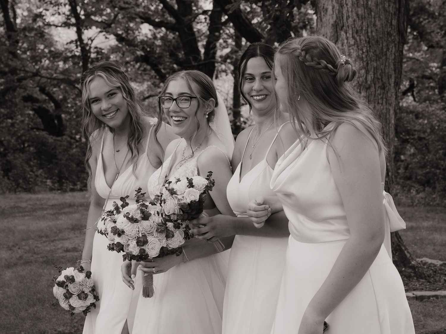 Black and white photo of bride and bridesmaids laughing together outdoors.
