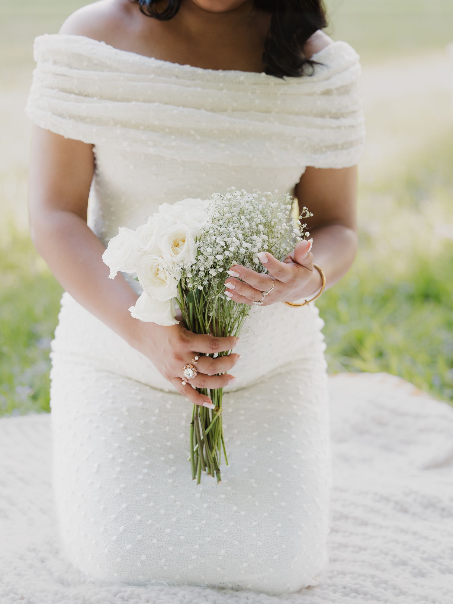 Bride in off-shoulder pearl white gown holding a delicate bouquet of roses and baby's breath.
