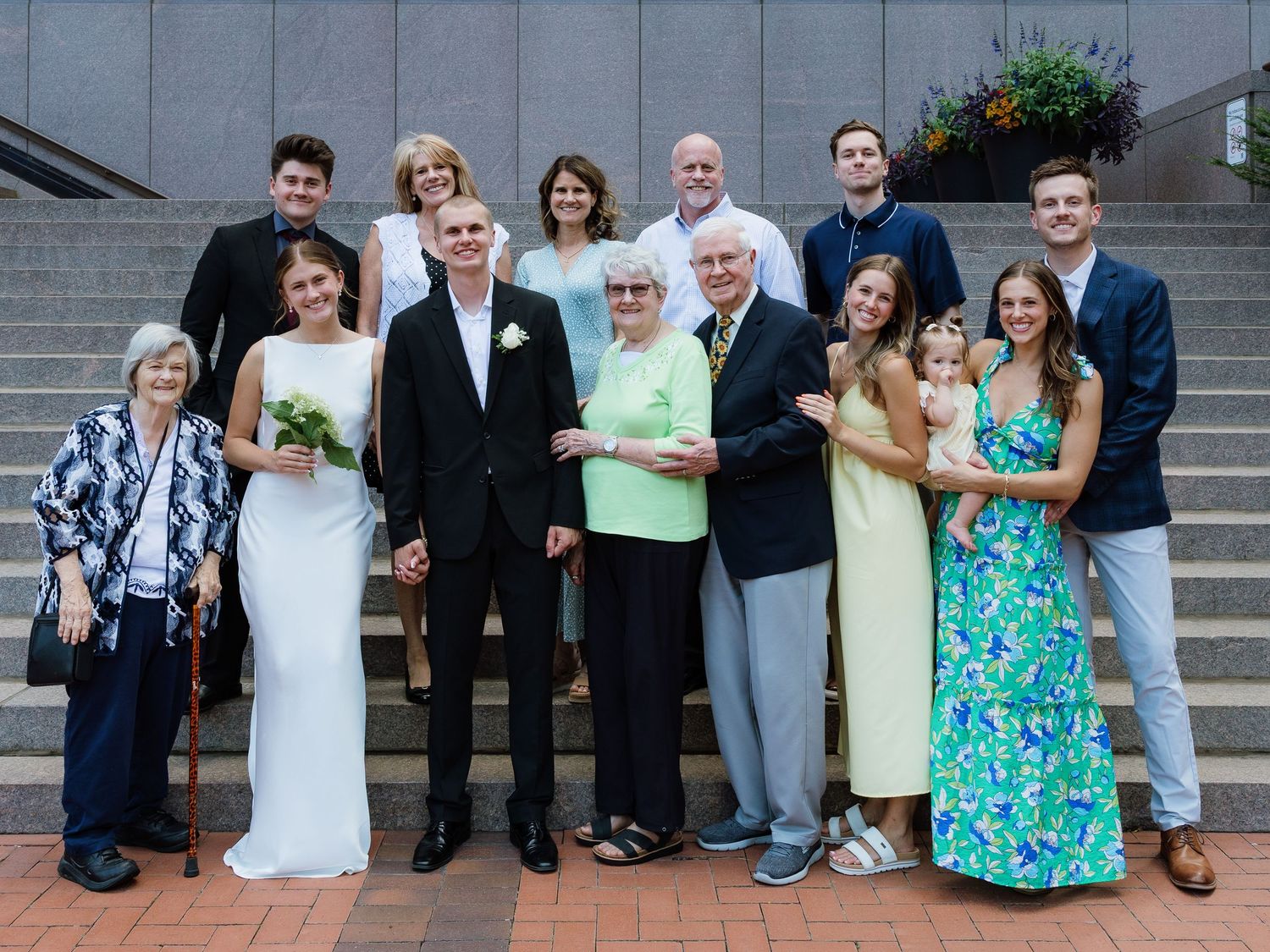 Family group photo at a wedding celebration on outdoor steps, featuring bride, groom, and relatives of all ages.