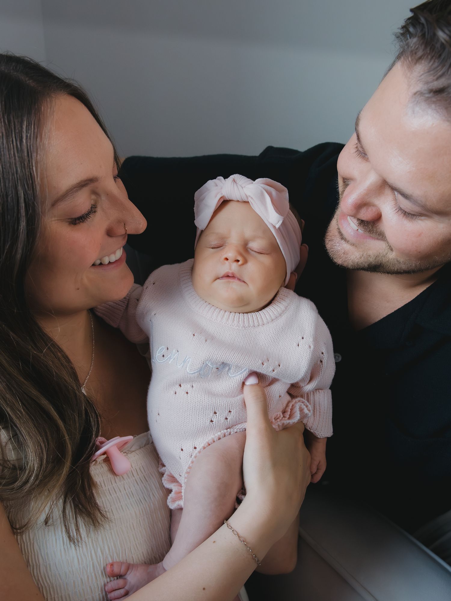 Happy parents lovingly gazing at their sleeping newborn baby dressed in pink at home.