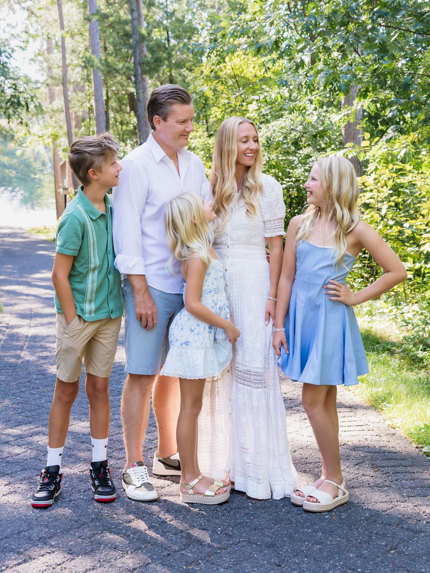 A family of five smiles together on a tree-lined path during an outdoor portrait session.