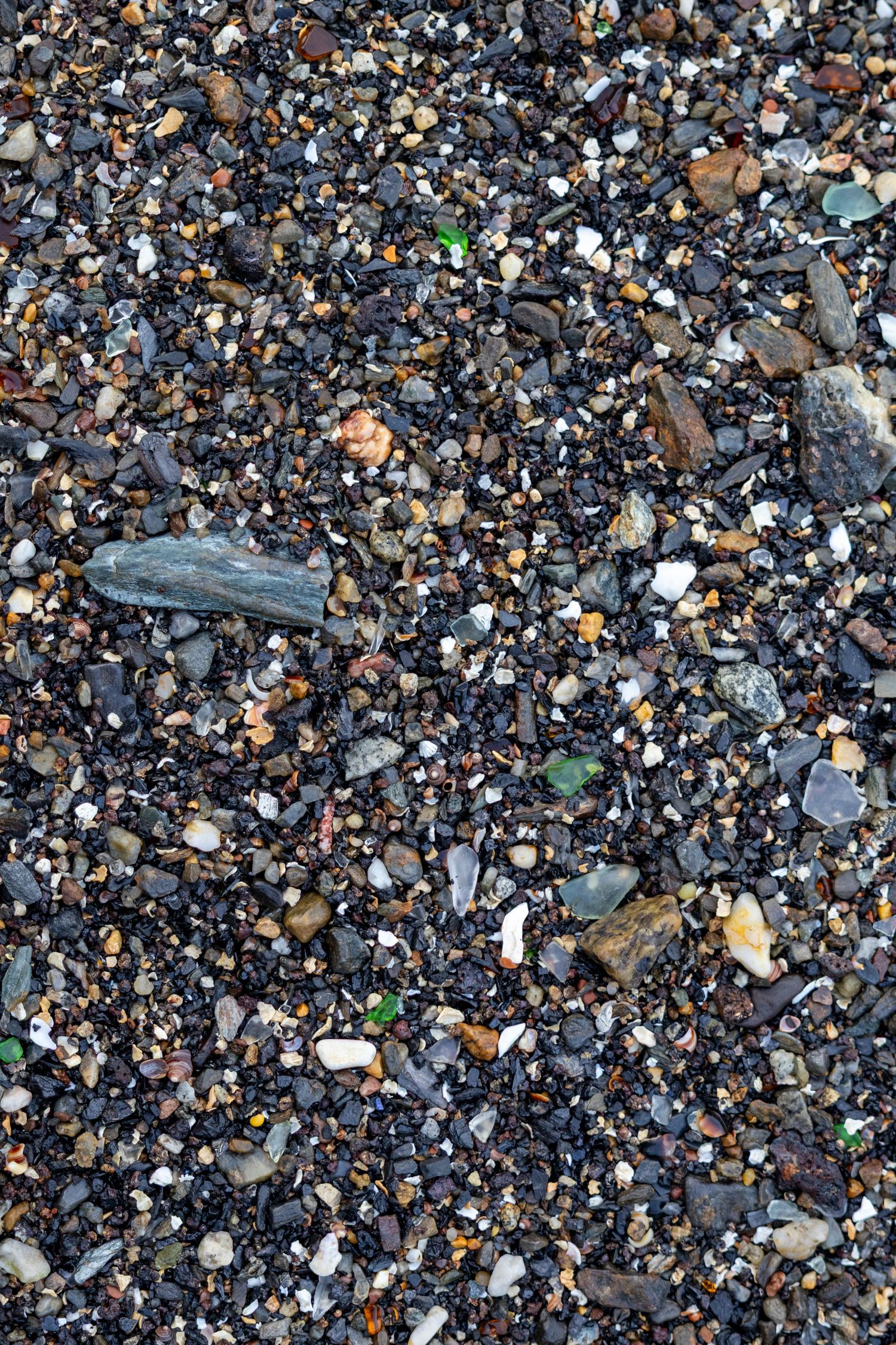 Close-up texture of dark mixed pebbles, gravel, and small colorful stones on a rocky beach.