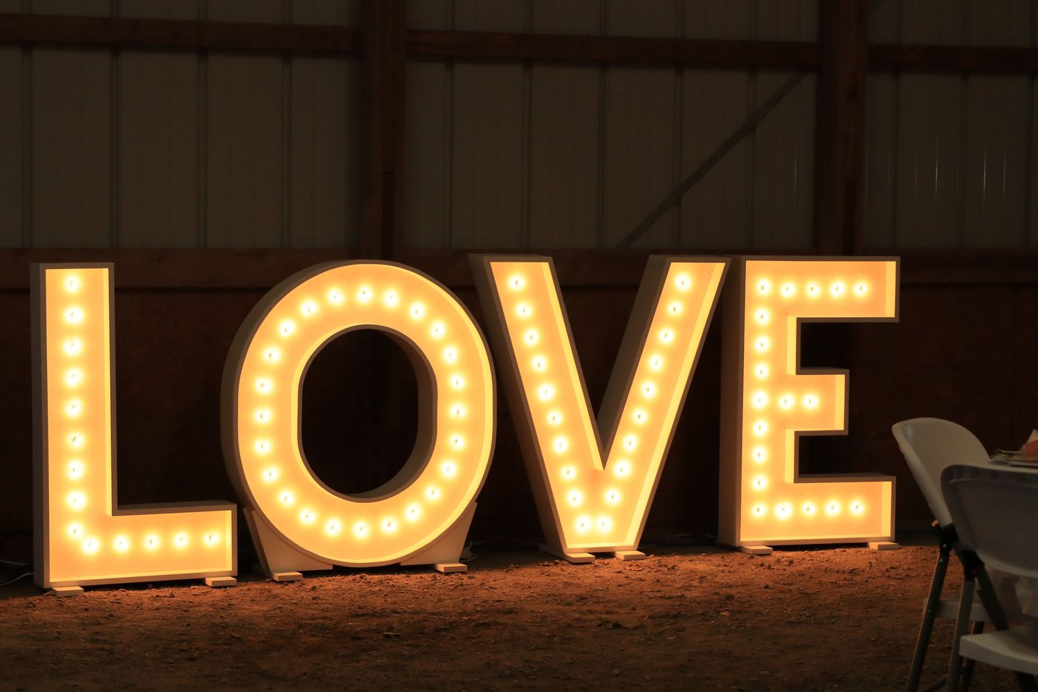 Illuminated marquee LOVE letters with light bulbs displayed inside a rustic barn venue at night.