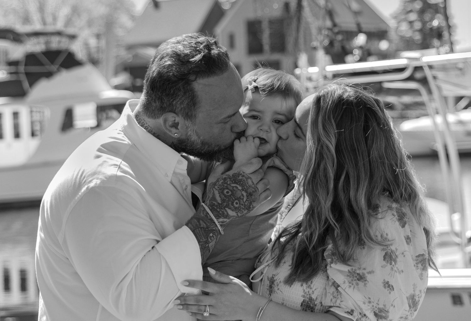 Black and white photo of couple kissing their young child outdoors near a marina.
