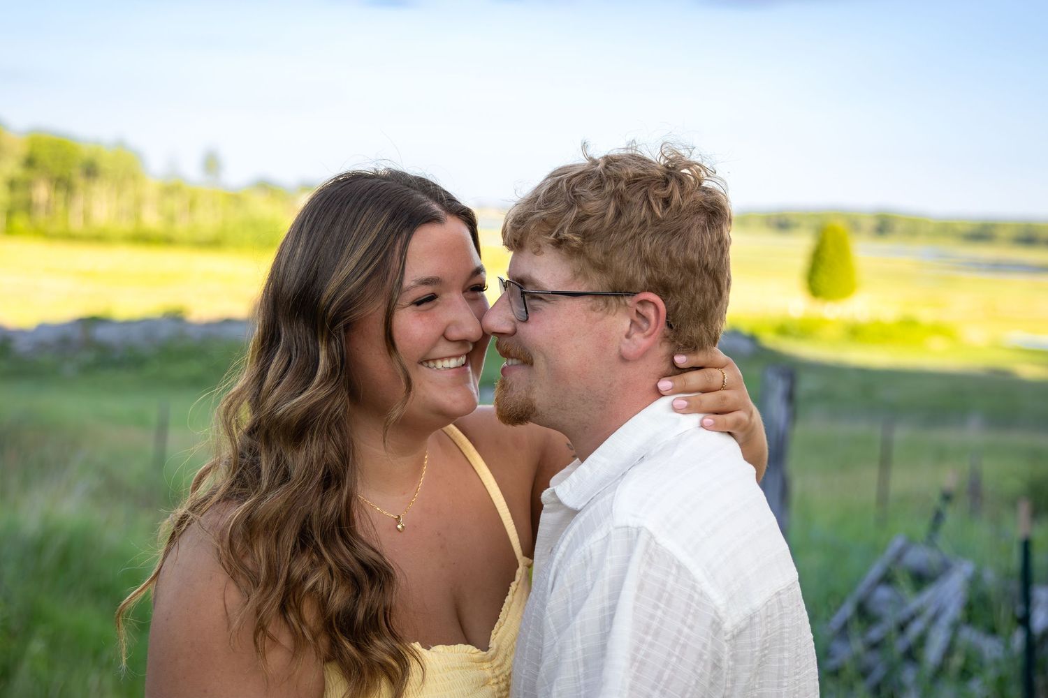 Happy couple smiling and embracing outdoors in a green field on a bright sunny day.