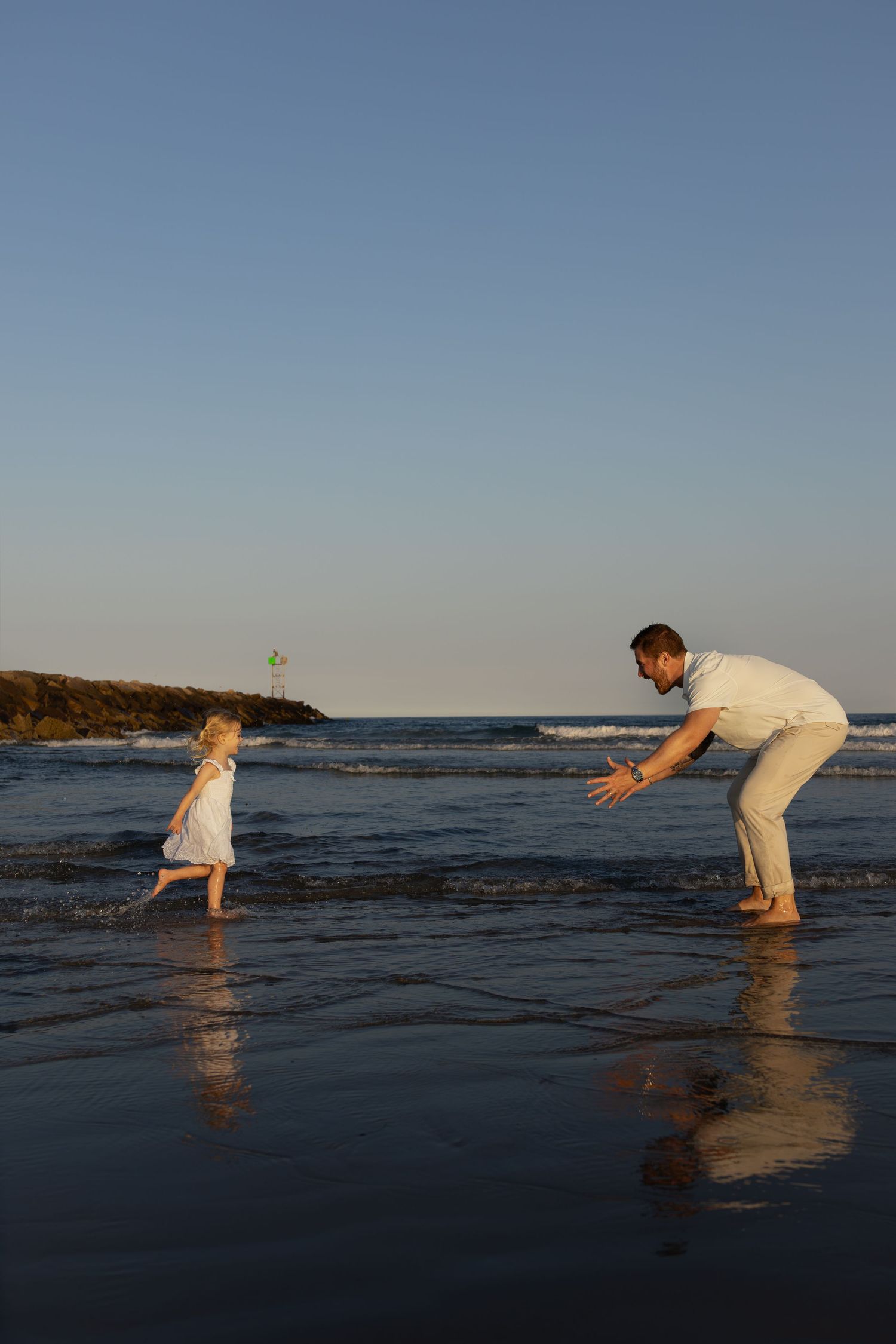 Father bending down with open arms as young daughter runs to him on a sunny beach at sunset.