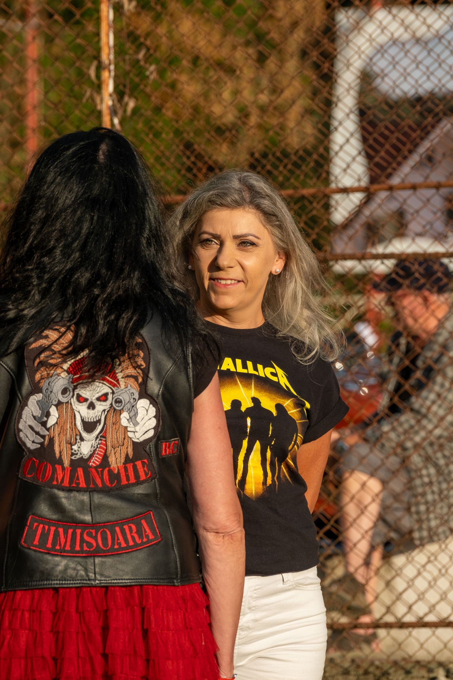 Woman with gray hair wearing Metallica t-shirt smiles at outdoor rock music festival.
