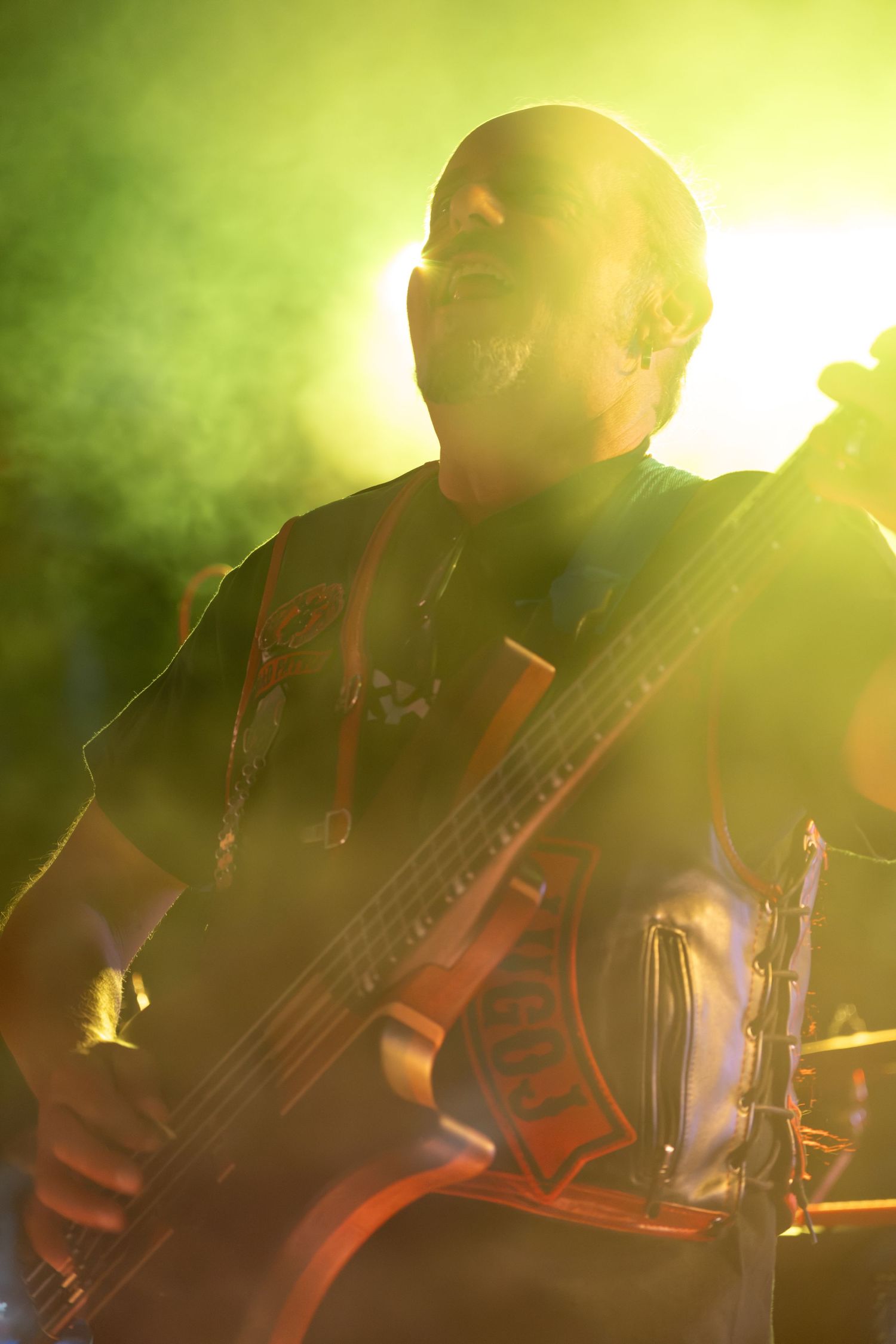 Bald bassist performs on stage surrounded by dramatic yellow and green smoke lighting effects.