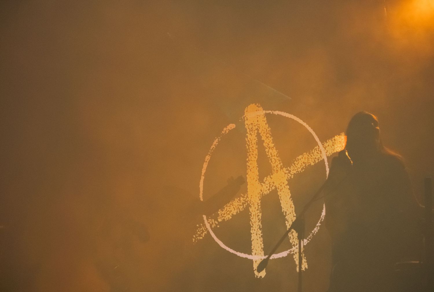 Anarchy symbol graffiti silhouetted against golden smoky haze at outdoor concert event.