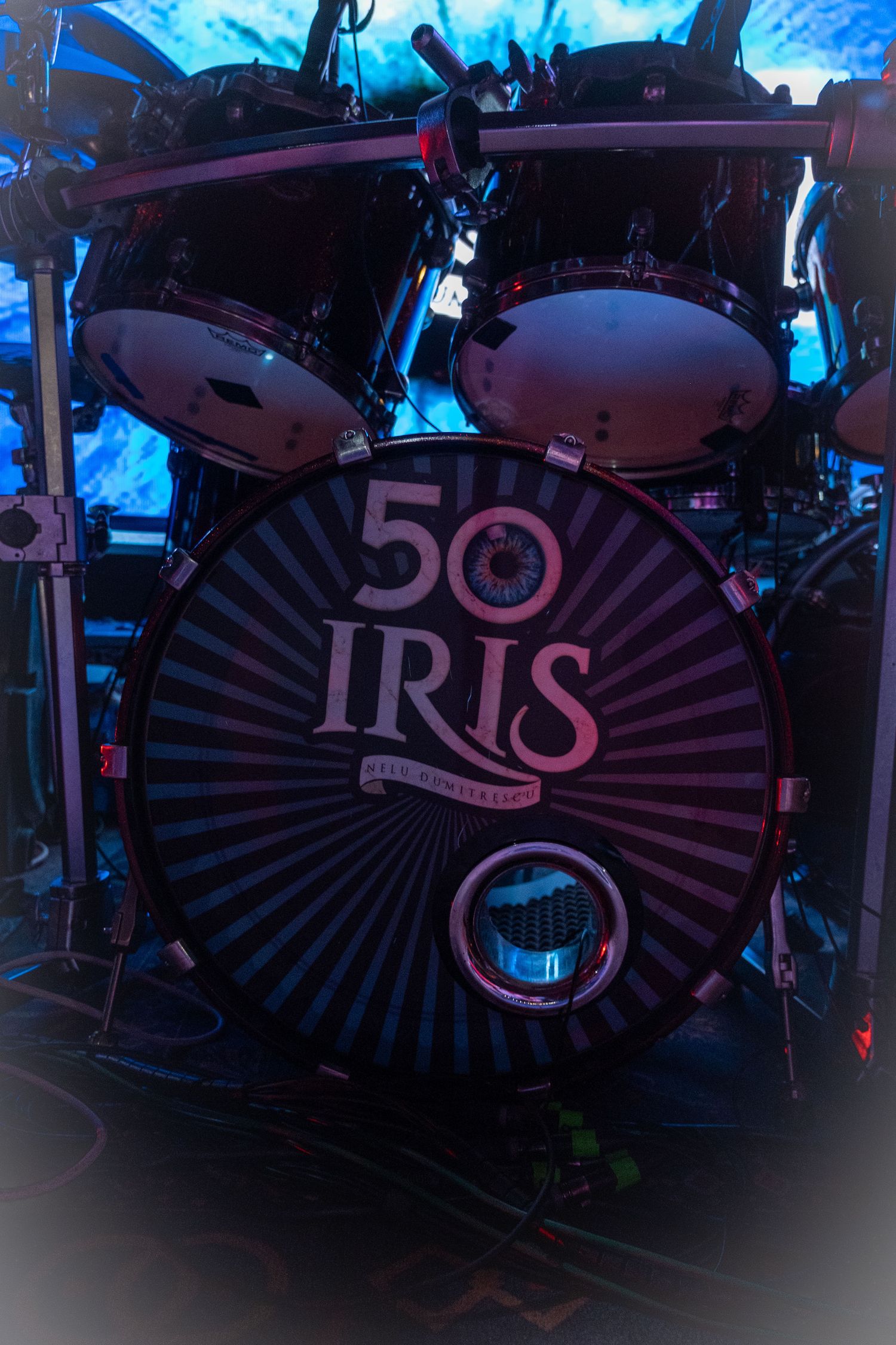 Iris band 50th anniversary drum kit with striped bass drum head on a dark concert stage.